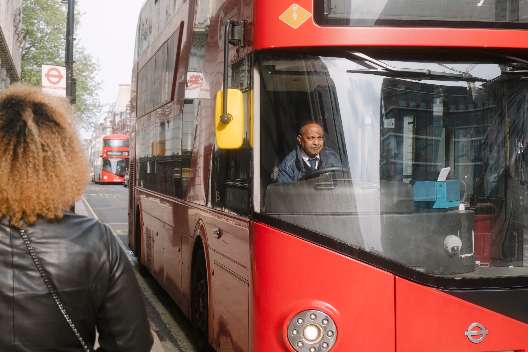 A London bus driver seen through the windshield of a red double-decker bus