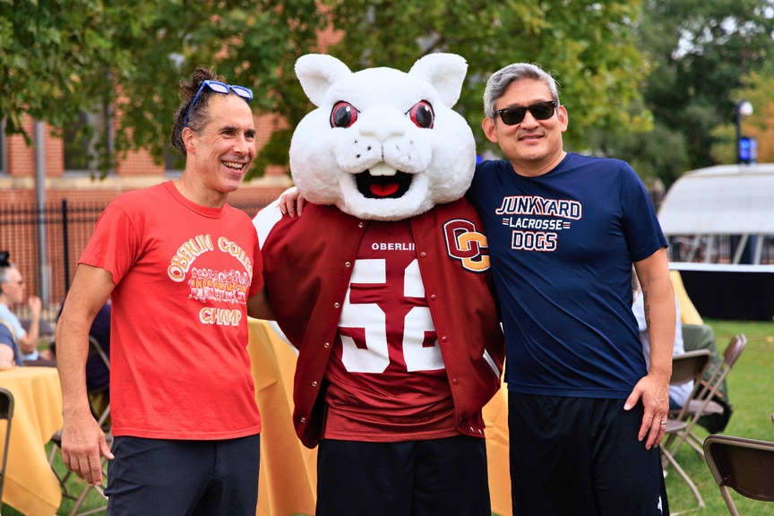 Two visitors posing with Oberlin's white squirrel mascot at an outdoor campus gathering