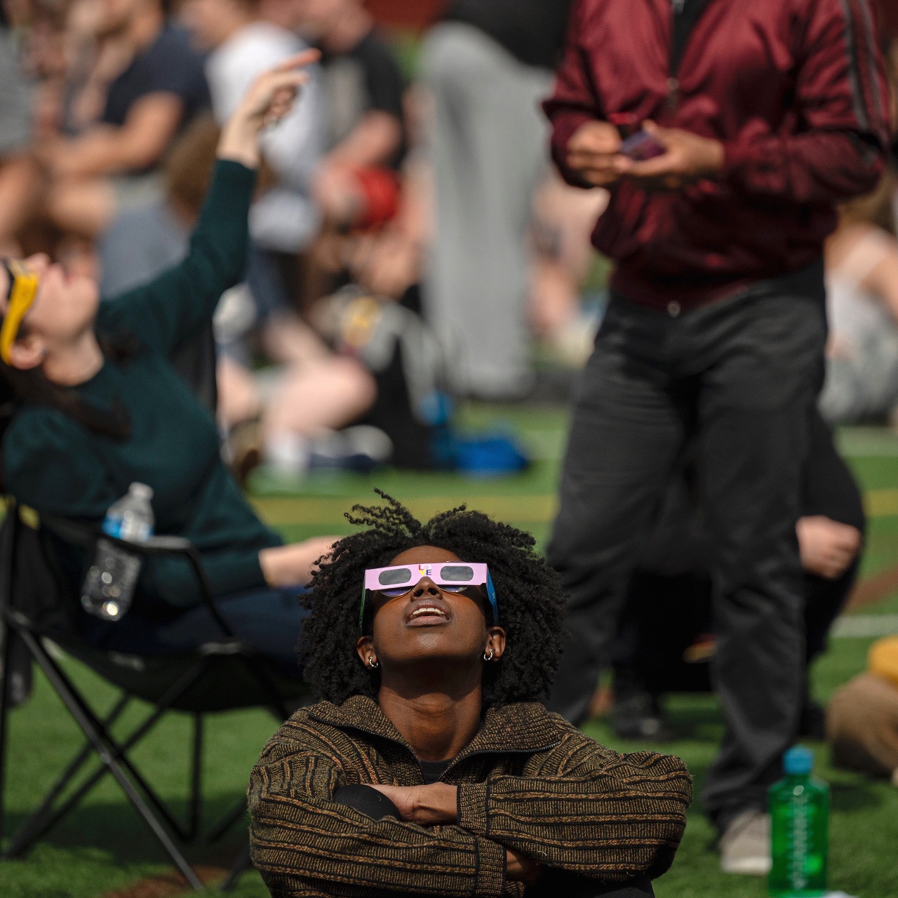 A viewer in pink eclipse glasses looking up during Oberlin's OCLIPSE gathering