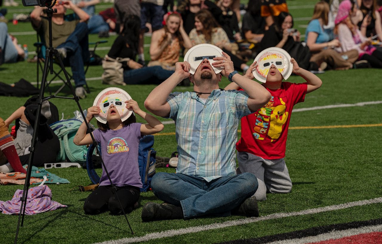 Students on the quad in eclipse glasses, two wearing mascot masks, April 2024